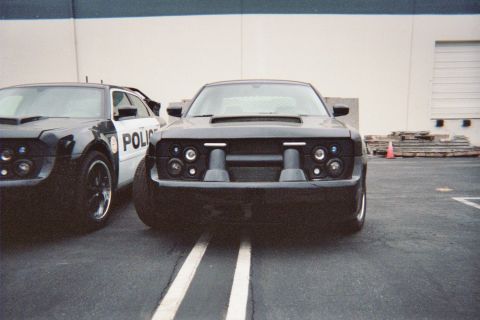 1990 Ford Bronco - Two black coupes with blacked-out faux grilles sit parked nose-out in a paved lot, one lettered 'POLICE'.
