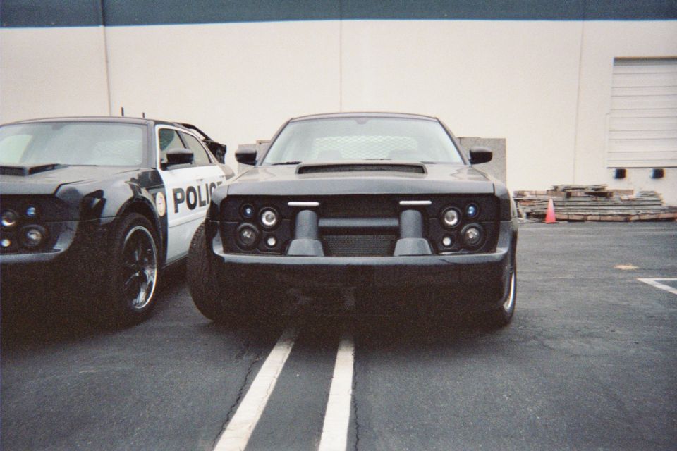 Front view of two black muscle cars with blacked-out grilles in a lot
