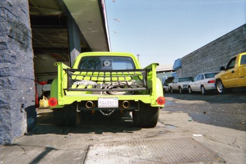1990 Ford Bronco - Rear view of a lime-green prerunner-style truck with a cargo net tailgate and dual exhaust parked in a shop bay, plate 5B68503.