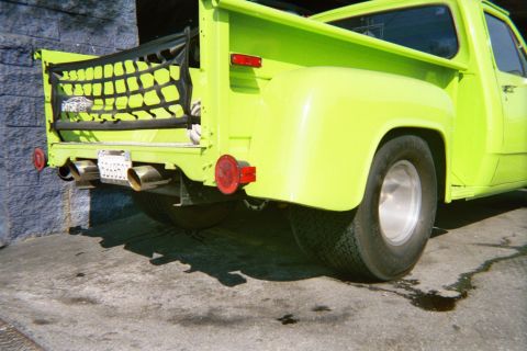 1990 Ford Bronco - Close rear corner of a bright lime-green stepside pickup showing a cargo-net tailgate, round taillights and dual exhaust tips.
