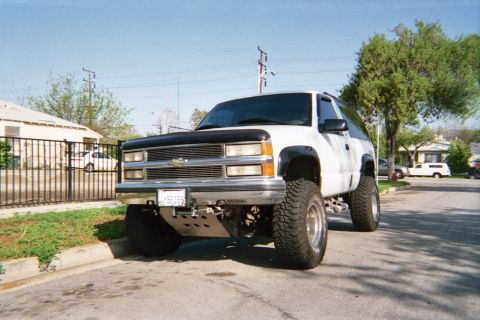 1990 Ford Bronco - Front three-quarter view of a white lifted two-door Chevrolet SUV with a chrome grille and bug shield parked in a driveway.