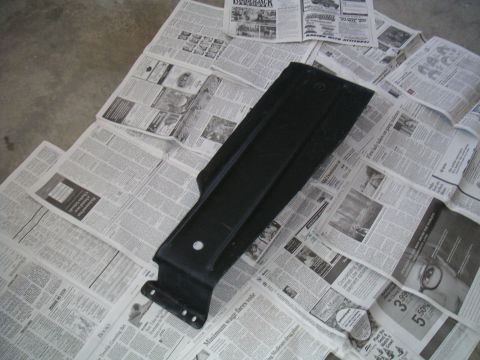 1994 Ford Bronco - A black plastic car part is placed on a spread of newspapers on a concrete floor.