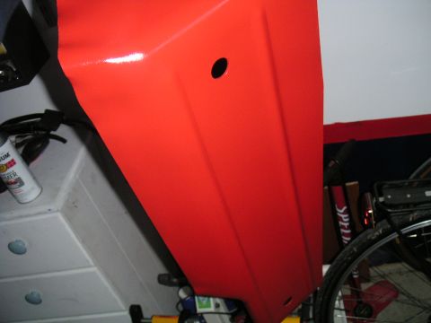 1994 Ford Bronco - A close-up shot focuses on a vibrant red vehicle panel, revealing a small, dark circular opening.