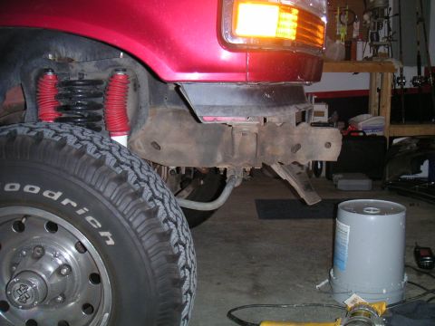 1994 Ford Bronco - Close-up of a red Ford Bronco's front fender and tire, showing suspension components and a detached bumper mount.
