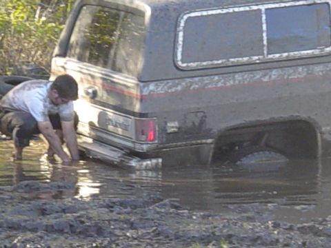 1989 Ford Bronco - A person wades in mud trying to free a large SUV that appears to be stuck.