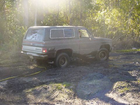 1989 Ford Bronco - Chevrolet K5 Blazer stuck in mud, with a yellow hose running to the front wheel.