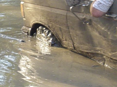 1989 Ford Bronco - This 1989 Ford Bronco is stuck deep in the mud and water, showing its side profile as the tires churn through the mire.