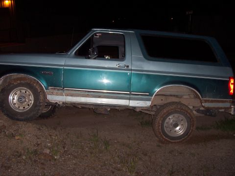 1996 Ford Bronco - A two-tone teal and gray Ford Bronco is seen from the side on a dirt path at night.