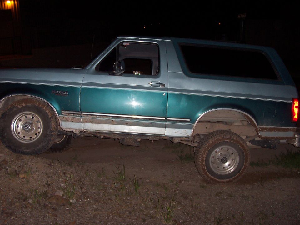Two-tone teal and gray Ford Bronco parked on dirt, side view