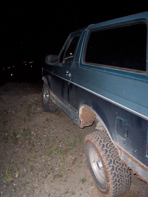 1996 Ford Bronco - This dark green SUV is parked on a dirt lot at night, with its tires showing off-road tread.