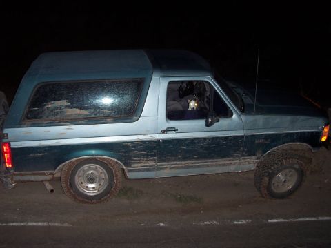 1996 Ford Bronco - Mud-covered Ford Bronco with a camper shell parked off-road at night.