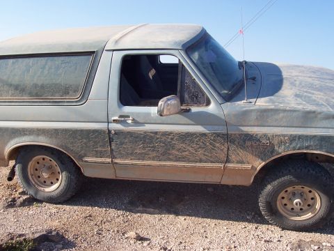 1996 Ford Bronco - Mud-covered 1996 Ford Bronco parked on a dirt road.