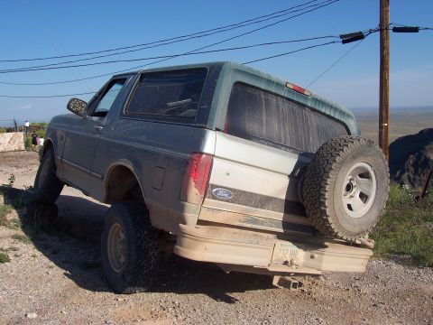 1996 Ford Bronco - A 1996 Ford Bronco is shown from the rear on a dirt road with one wheel elevated.