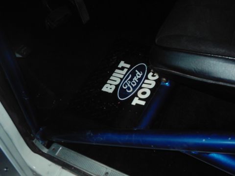 1978 Ford Bronco - The interior of a vehicle features a "Built Ford Tough" floor mat and a blue roll cage.