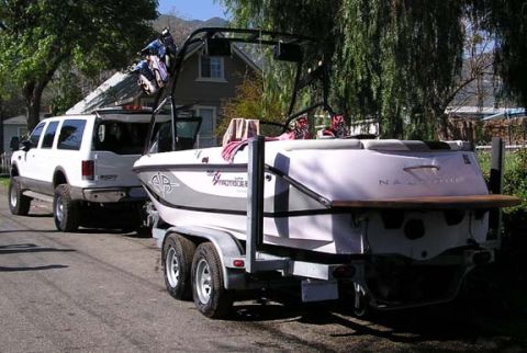 2002 Ford Excursion - A white SUV is parked on a street, towing a boat on a trailer. The SUV's rear hatch is open.