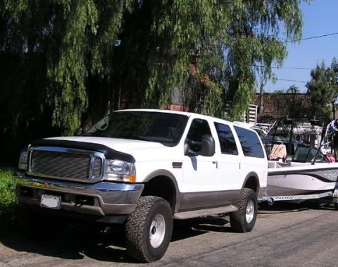 2002 Ford Excursion - A white Ford Excursion is parked on a street, towing a boat on a trailer.