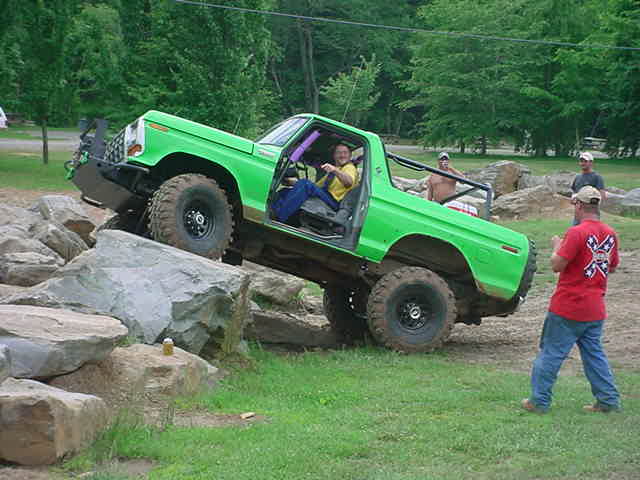 Driver in green lifted Ford Bronco descending a rock ledge, spectator in foreground