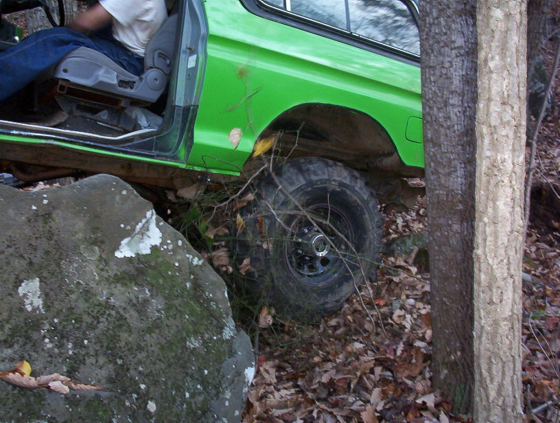 Close view of green Bronco rear wheel and quarter panel lifted off a mossy boulder on a trail