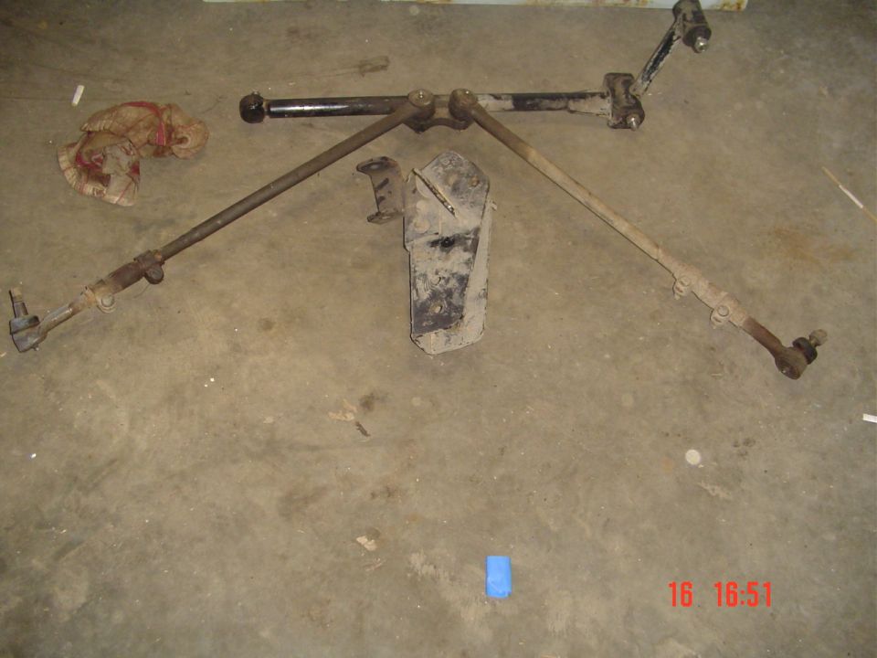 Used steering linkage with tie rod ends and steering stabilizer laid out on a concrete floor