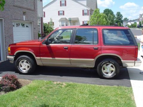 1992 Ford Explorer - Side view of a red 1992 Ford Explorer parked on a paved driveway next to a brick house.