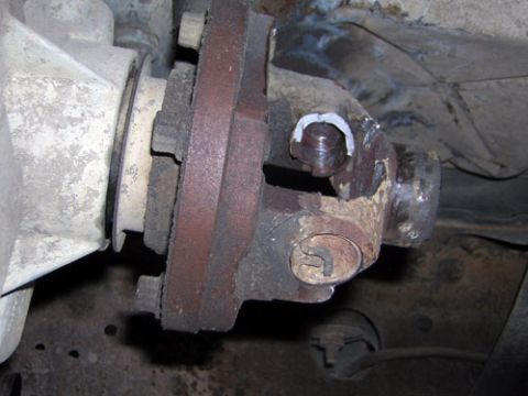 1995 Ford Bronco - Underbody close-up of a driveshaft U-joint and yoke bolted to a rusty differential or transfer case output flange, with a fresh white greas…