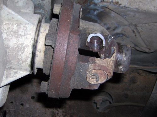Rusty driveshaft U-joint and yoke bolted to an output flange underneath a truck, with fresh grease visible