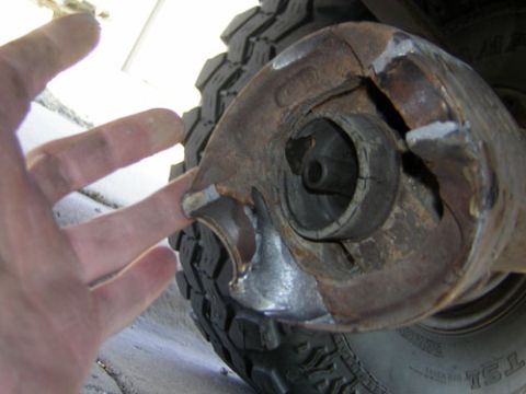 1995 Ford Bronco - Close-up of a badly cracked and broken cast housing, likely a differential or axle-end casting, held up beside a knobby off-road tire, with…