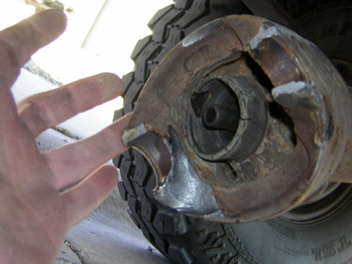 Hand pointing at cracked and broken rusty axle housing casting next to an off-road tire