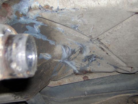 1995 Ford Bronco - Close-up underbody shot of a dusty floor pan and frame area with heat-tinted blue weld beads laid over a repaired seam and gusset. A polish…
