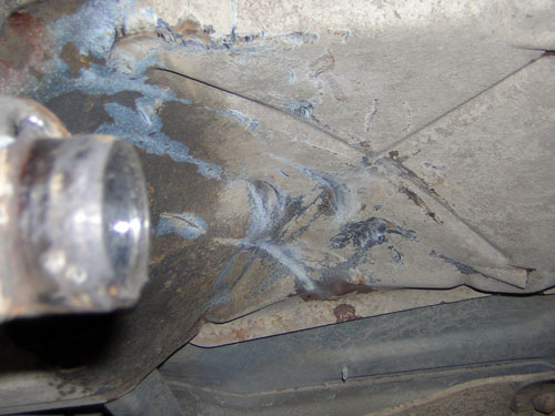 Underbody weld repair with blue heat-tinted beads next to an exhaust pipe