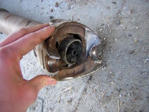 1995 Ford Bronco - A hand holds the end of a steel driveshaft over a concrete driveway, showing the U-joint yoke and the worn universal-joint bearing cup.