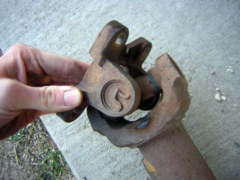 1995 Ford Bronco - A hand holds a rusty driveshaft U-joint yoke up to the camera on a concrete driveway, showing the cross and cap seated in the yoke ears. Su…