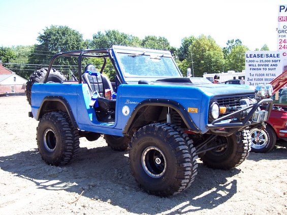 Blue lifted early Ford Bronco with roll cage and big tires at a car show