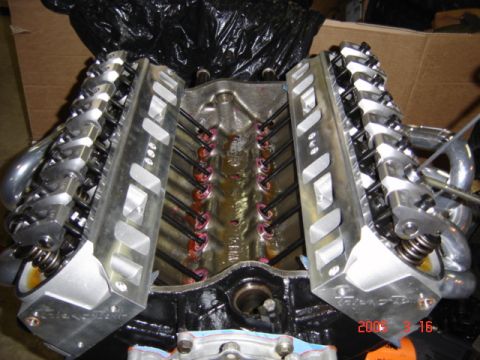 1990 Ford Bronco - Top-down view of an assembled V8 short block on a stand with both aluminum cylinder heads installed, valve covers off, exposing the rocker…