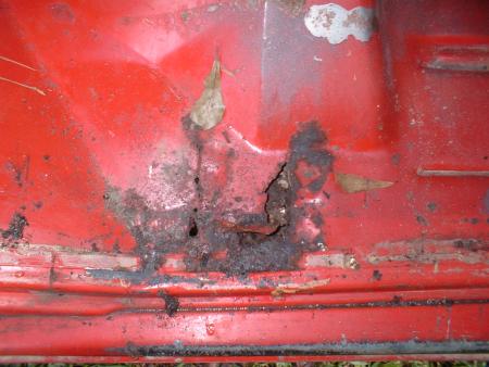 1978 Ford Bronco - Close-up of rusted red metal panel, likely from a vehicle's exterior, with debris.