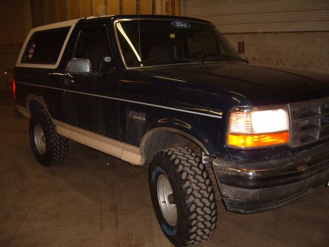 1993 Ford Bronco - A dark blue 1993 Ford Bronco with a white removable top is parked indoors.