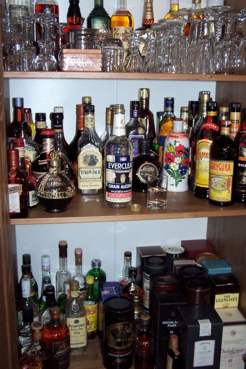 1990 Ford Bronco - A collection of alcoholic beverages and barware displayed on wooden shelves.