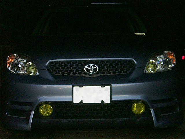 Front end of dark Toyota Matrix at night with yellow fog lights lit
