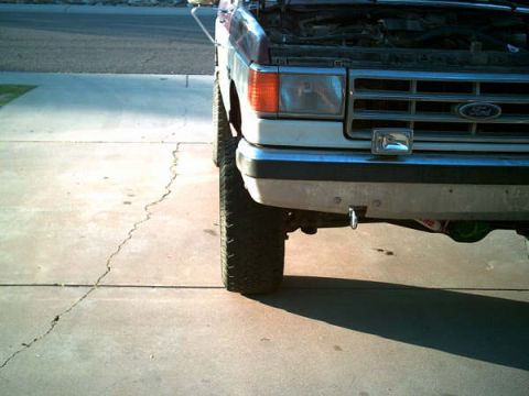 1988 Ford Bronco - A white and maroon Ford Bronco is shown from the front with its hood up, parked on a cracked concrete surface.