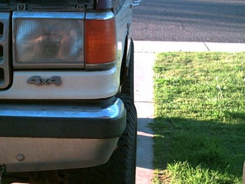 1988 Ford Bronco - Close-up of the front corner of a 1988 Ford Bronco, showing the headlight and 4x4 emblem.