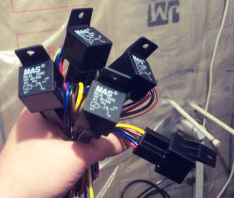 1985 Ford LTD Crown Victoria - Several automotive relays with wiring are held in a hand against a textured background.