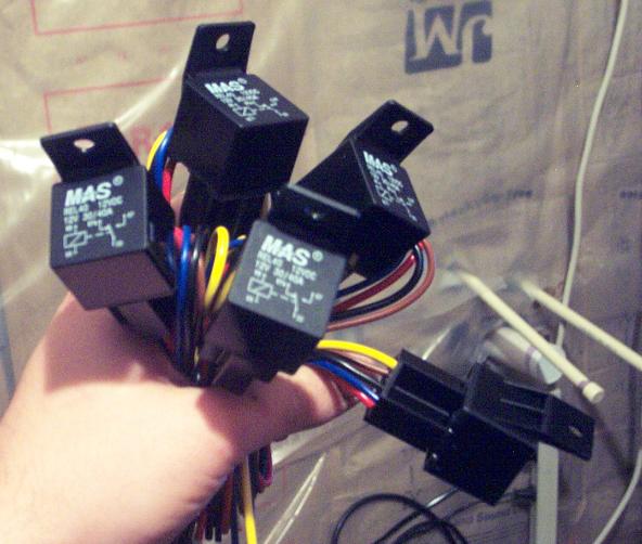 Hand holding multiple black automotive relays with wiring harnesses