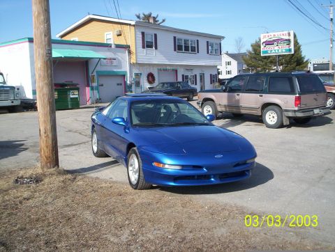 1997 Ford Probe - A blue 1997 Ford Probe is parked in front of a building with a sign for "Jean & Luke's Body Shop".