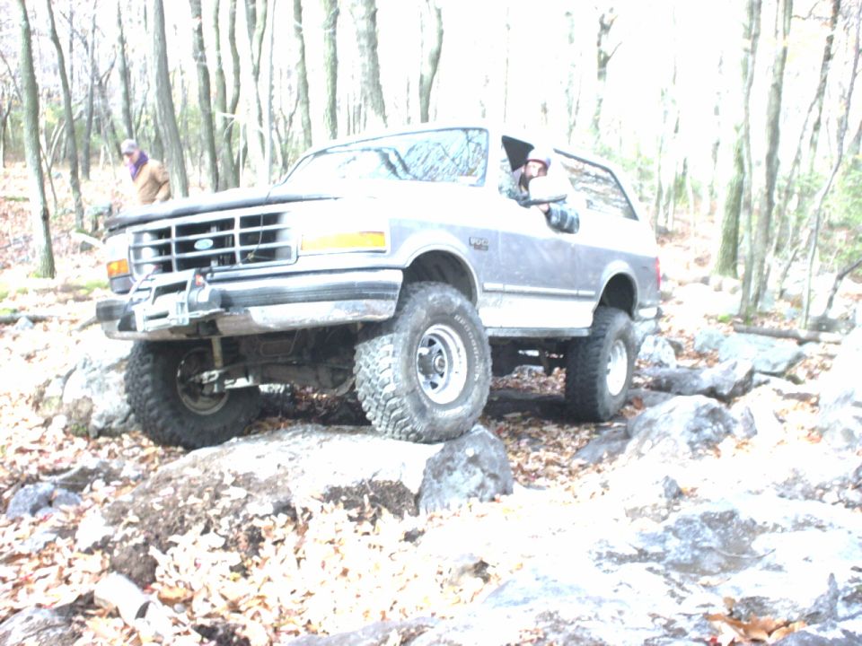 Gray Ford Bronco with lifted suspension driving over rocks in a wooded area