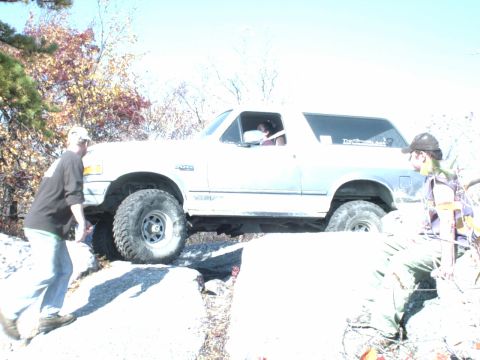 1995 Ford Bronco - A white 1995 Ford Bronco navigates a rocky trail, demonstrating its off-road capabilities.