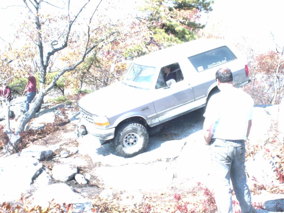 1995 Ford Bronco climbing a rocky hill with people watching