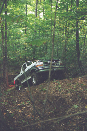 1995 Ford Bronco - A two-tone green and white Ford F-Series truck navigates a wooded area.