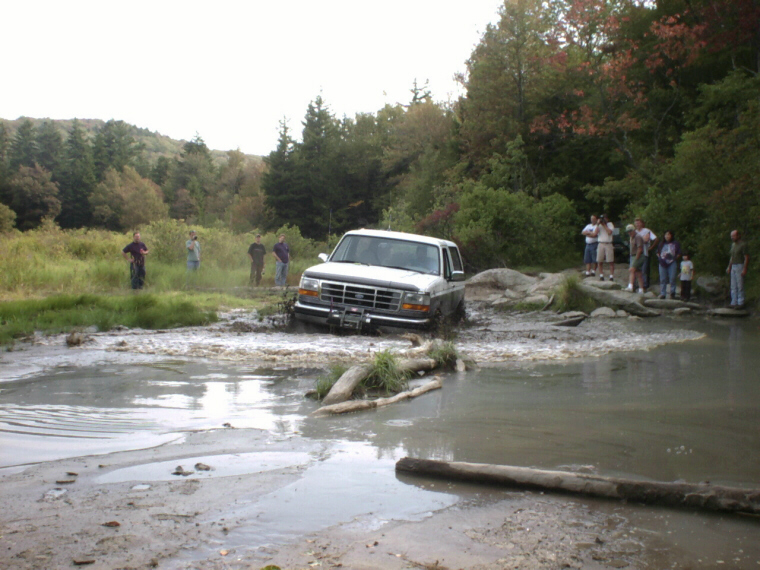 1995 Ford Bronco stuck in a muddy water crossing with people watching