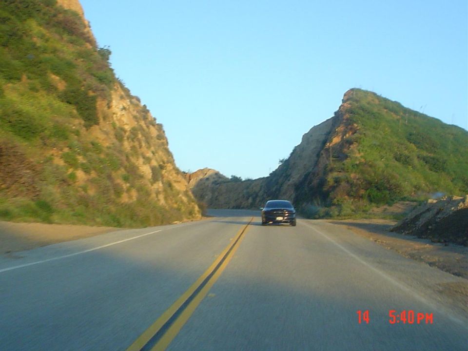 Car driving on a road between hills. Time stamp 14 5:40PM visible