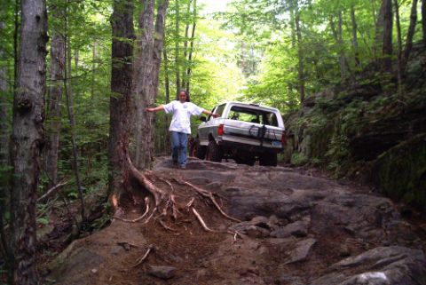 1995 Ford Bronco - A white 1995 Ford Bronco tackles a challenging rocky path through a dense forest.